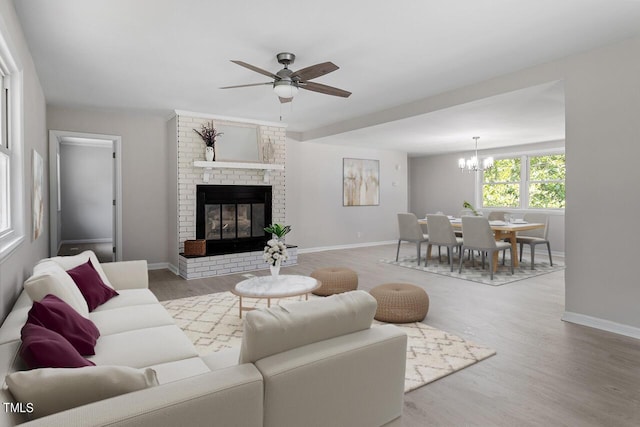 living room with a brick fireplace, ceiling fan with notable chandelier, and light hardwood / wood-style flooring