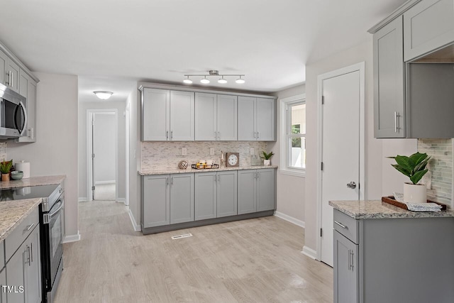 kitchen featuring light hardwood / wood-style floors, light stone counters, appliances with stainless steel finishes, and gray cabinetry