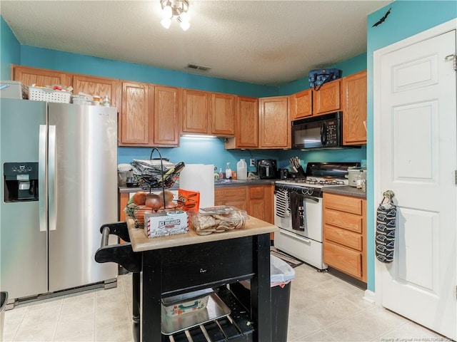 kitchen featuring white range with gas cooktop, stainless steel fridge with ice dispenser, and a textured ceiling