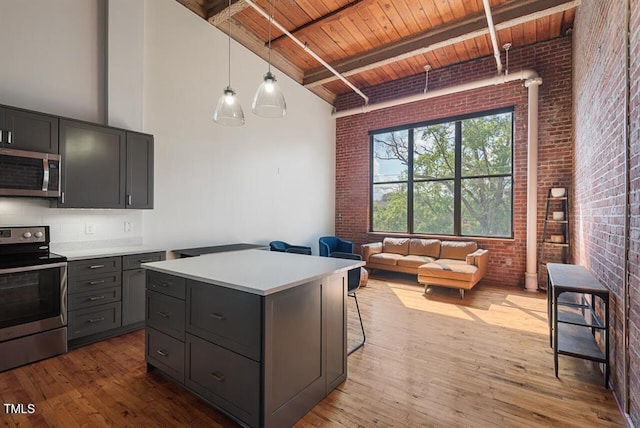 kitchen with brick wall, a kitchen island, beamed ceiling, appliances with stainless steel finishes, and wooden ceiling