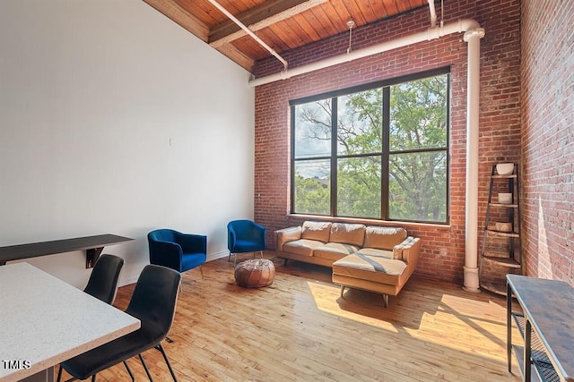 interior space with wood ceiling, light hardwood / wood-style floors, a towering ceiling, beamed ceiling, and brick wall