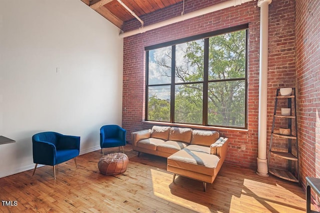 living area featuring beamed ceiling, wooden ceiling, plenty of natural light, and brick wall