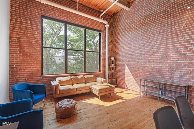 living room featuring beamed ceiling, brick wall, a towering ceiling, and wood ceiling