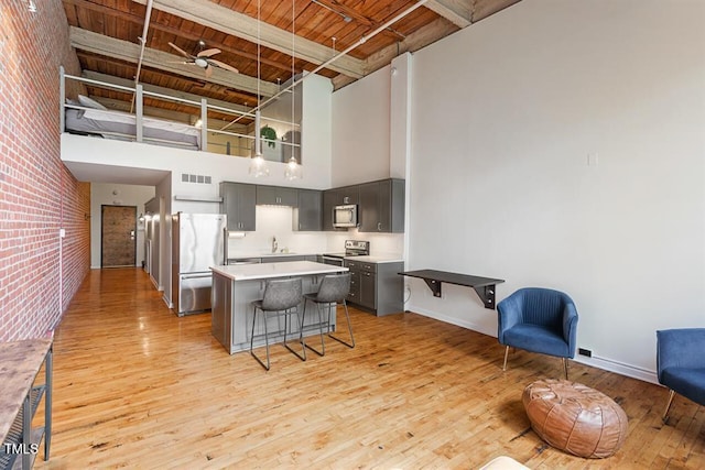 kitchen featuring a high ceiling, stainless steel appliances, brick wall, wood ceiling, and beamed ceiling