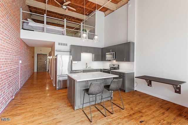 kitchen featuring a high ceiling, brick wall, stainless steel appliances, beam ceiling, and wooden ceiling