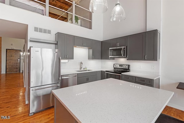 kitchen with sink, light stone counters, a high ceiling, pendant lighting, and appliances with stainless steel finishes