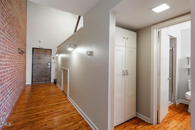 hall with light wood-type flooring and brick wall