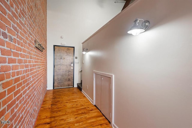 corridor with light hardwood / wood-style flooring, a towering ceiling, and brick wall