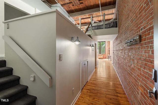 hall featuring a high ceiling, brick wall, wood ceiling, wood-type flooring, and beamed ceiling