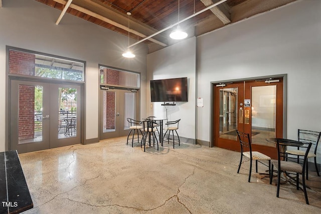 interior space featuring beamed ceiling, a towering ceiling, french doors, concrete flooring, and wood ceiling