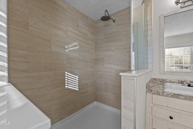 bathroom with tiled shower, vanity, and a textured ceiling