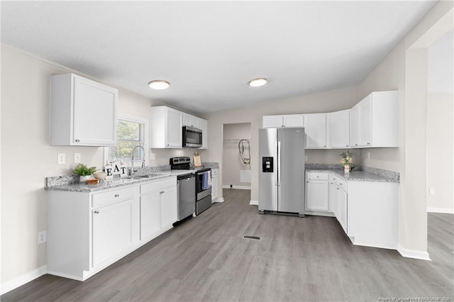 kitchen with appliances with stainless steel finishes, white cabinetry, light stone counters, and sink