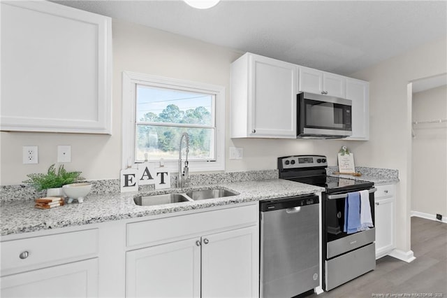 kitchen with light stone counters, light wood-type flooring, white cabinetry, appliances with stainless steel finishes, and sink