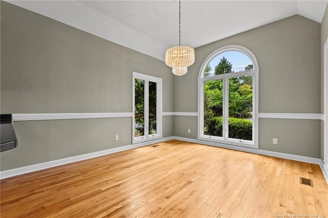 spare room featuring a chandelier, vaulted ceiling, and light hardwood / wood-style flooring