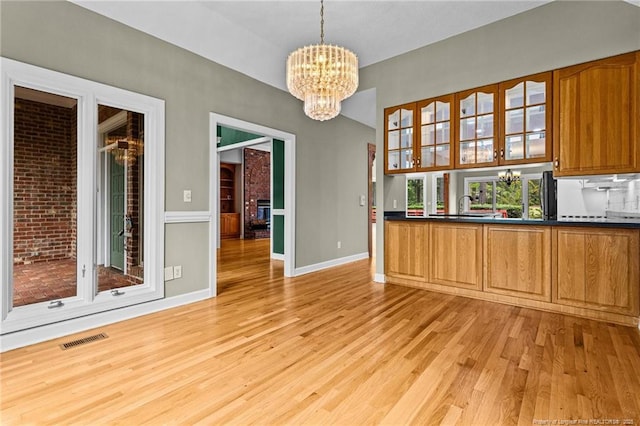 kitchen with sink, decorative light fixtures, a fireplace, light wood-type flooring, and a notable chandelier