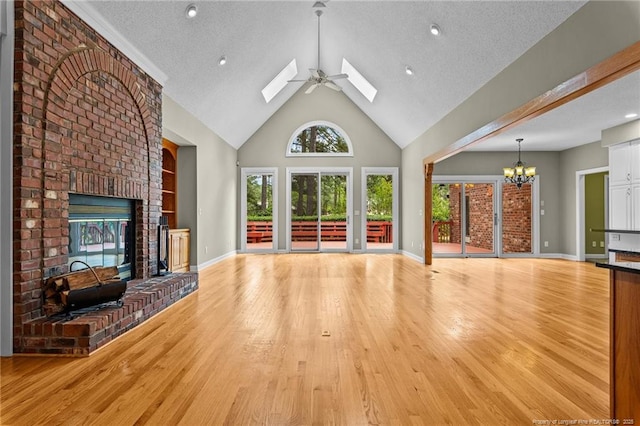 unfurnished living room with light hardwood / wood-style floors, a skylight, high vaulted ceiling, a fireplace, and ceiling fan with notable chandelier