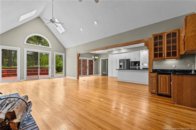 living room with light hardwood / wood-style flooring, high vaulted ceiling, a skylight, ceiling fan with notable chandelier, and sink