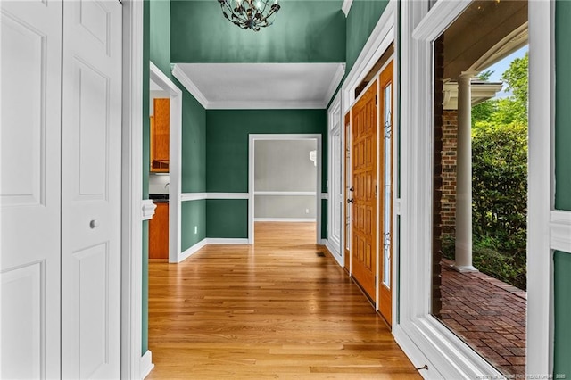 corridor featuring light hardwood / wood-style floors, crown molding, a chandelier, and decorative columns