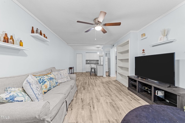 living room with built in shelves, ornamental molding, ceiling fan, and light wood-type flooring