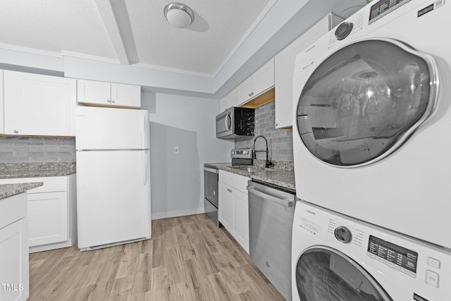 kitchen featuring white cabinetry, sink, stacked washer and dryer, stainless steel appliances, and a textured ceiling