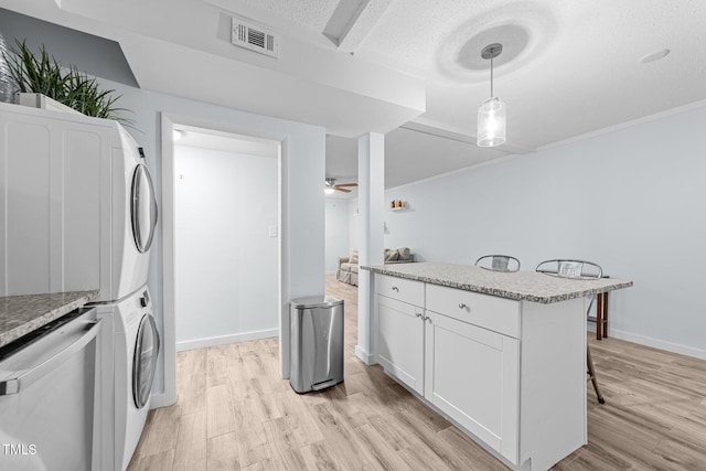 clothes washing area featuring a textured ceiling, light hardwood / wood-style floors, ceiling fan, and stacked washer / dryer