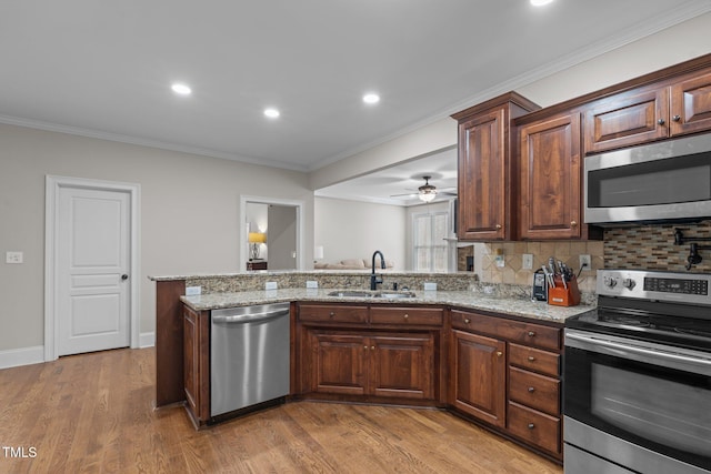 kitchen with stainless steel appliances, light stone counters, sink, light hardwood / wood-style flooring, and backsplash