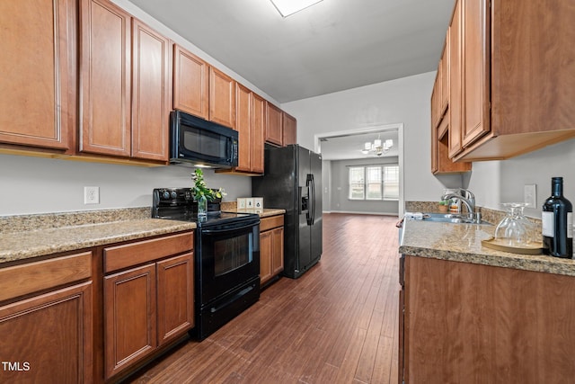 kitchen featuring a notable chandelier, dark hardwood / wood-style flooring, light stone countertops, black appliances, and sink