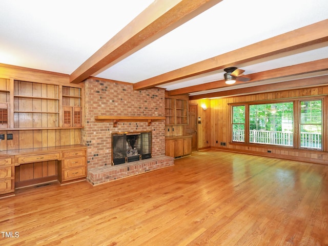 unfurnished living room with a brick fireplace, built in desk, wooden walls, and light wood-type flooring