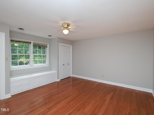 empty room with ceiling fan, wood-type flooring, and a textured ceiling