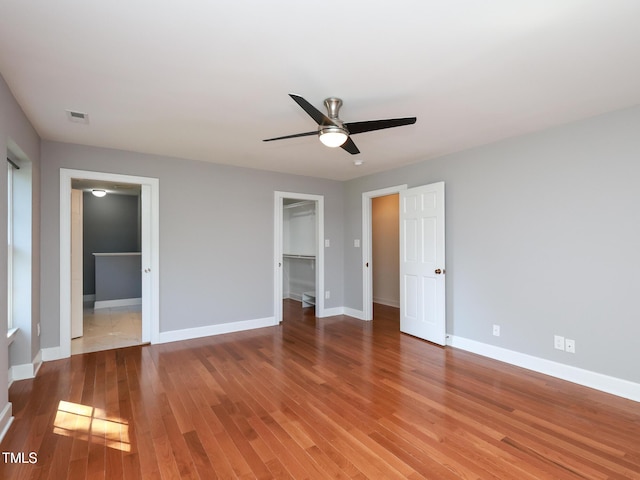 unfurnished bedroom with hardwood / wood-style floors, a walk in closet, a closet, and ceiling fan