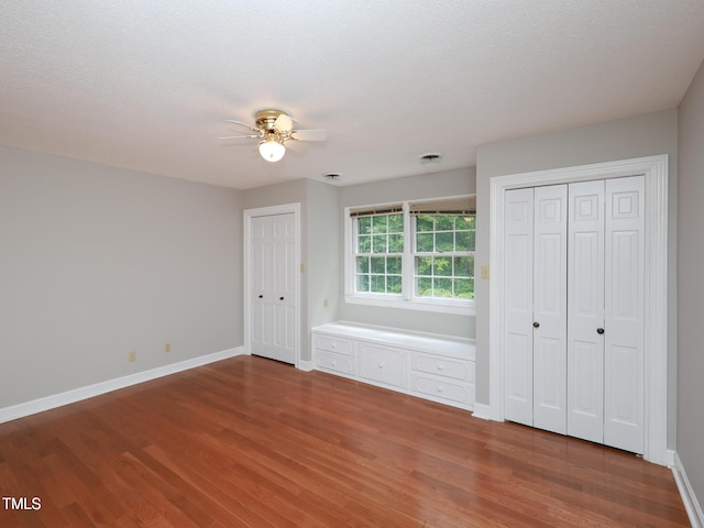 unfurnished bedroom with multiple closets, ceiling fan, a textured ceiling, and hardwood / wood-style flooring