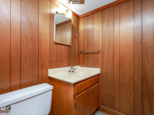 bathroom featuring vanity, wood walls, and toilet