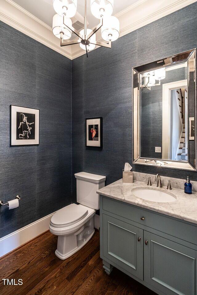 bathroom with hardwood / wood-style floors, vanity, a notable chandelier, ornamental molding, and toilet