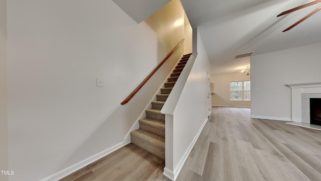 stairs with hardwood / wood-style floors, a high end fireplace, and ceiling fan with notable chandelier