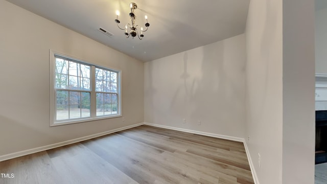 empty room with light hardwood / wood-style floors and an inviting chandelier