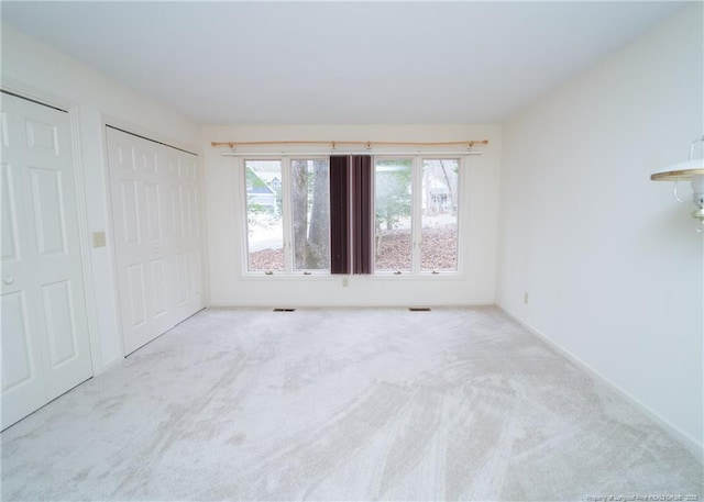 unfurnished bedroom featuring multiple closets and light colored carpet