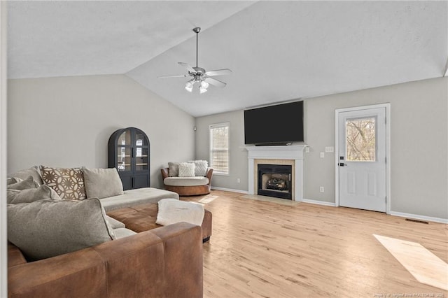 living room with a tiled fireplace, ceiling fan, vaulted ceiling, and light hardwood / wood-style flooring