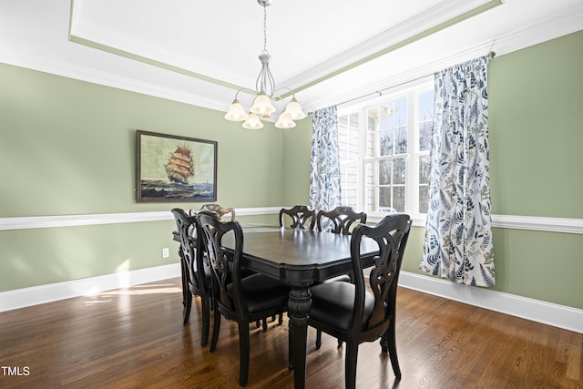 dining space with an inviting chandelier, a tray ceiling, dark wood-type flooring, and ornamental molding