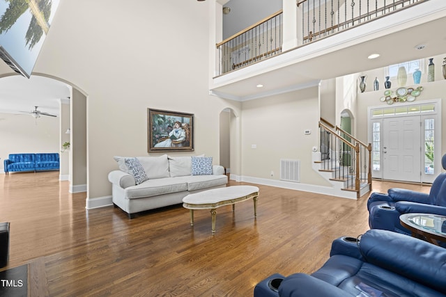 living room featuring dark wood-type flooring, ceiling fan, and a high ceiling