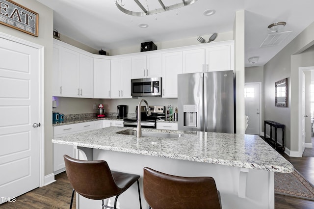 kitchen with white cabinetry, stainless steel appliances, dark hardwood / wood-style floors, light stone counters, and a center island with sink