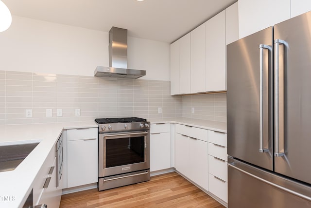 kitchen featuring appliances with stainless steel finishes, exhaust hood, light wood-type flooring, white cabinets, and backsplash