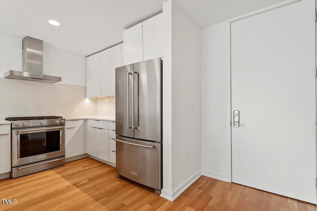 kitchen with light wood-style floors, wall chimney exhaust hood, appliances with stainless steel finishes, and light countertops