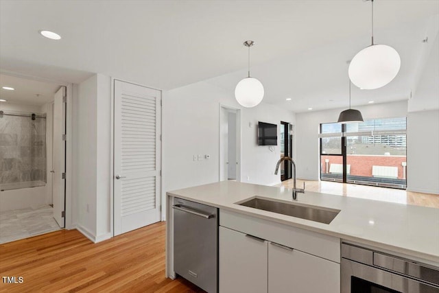 kitchen with white cabinets, light countertops, a sink, and dishwasher