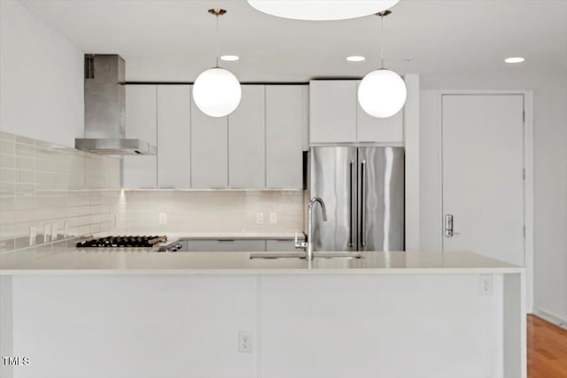 kitchen featuring wall chimney exhaust hood, appliances with stainless steel finishes, decorative backsplash, and a sink