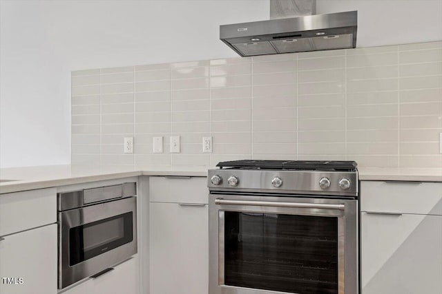 kitchen featuring wall chimney exhaust hood, stainless steel gas range oven, light countertops, and decorative backsplash