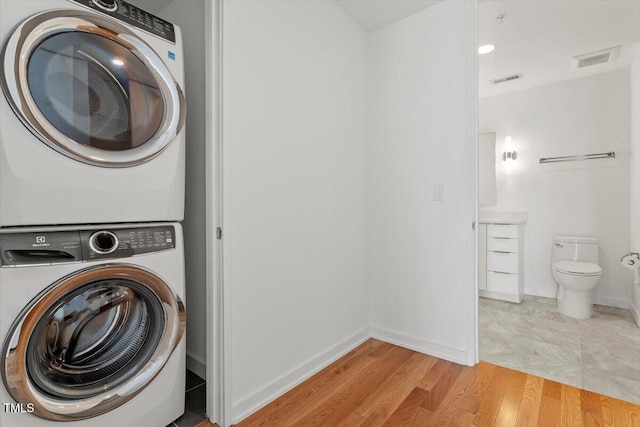 clothes washing area with baseboards, light wood-style flooring, visible vents, and stacked washer / drying machine