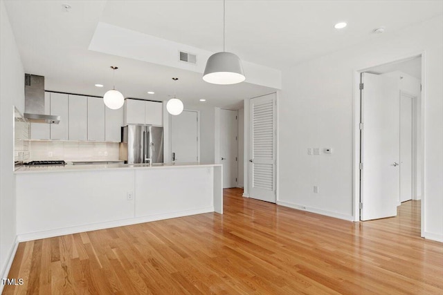 kitchen with wall chimney range hood, light wood-style flooring, high end refrigerator, and visible vents