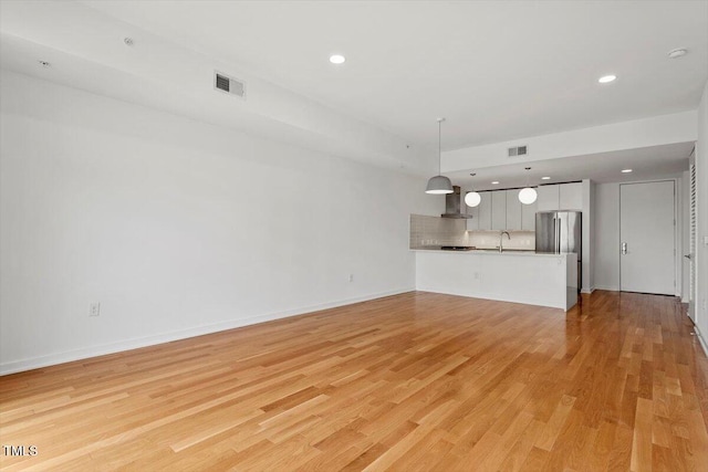 unfurnished living room with light wood-style flooring, a sink, visible vents, and baseboards