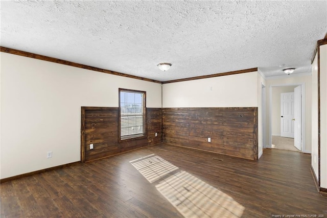 spare room featuring ornamental molding, dark hardwood / wood-style flooring, wood walls, and a textured ceiling