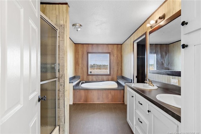 bathroom with a textured ceiling, plus walk in shower, wood walls, and vanity